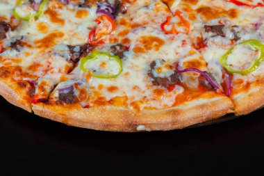 Siyah arka planda et ve sebzeli pizza dilimi.