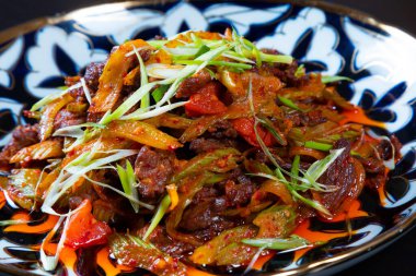 Siyah arka planda doğranmış et ve sebzelerle kaplanmış tabak. Asya mutfağı