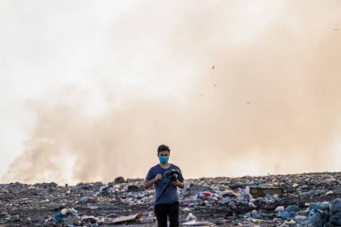 Çöplerle ve yanan çöp yığınlarıyla dolu bir çöp sahasında fotoğrafçı.