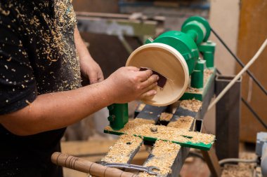 Torna tezgahında zımpara kağıdı kullanarak ahşap ürünü zımparalamaya yakın olan kişi.