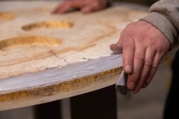 Closeup of person sanding wooden table using sandpaper in workshop