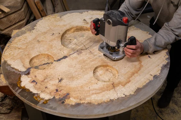 Atölyedeki ahşap bir masada ahşap yönlendiriciyle çalışan bir adam.