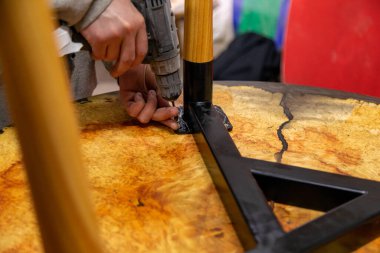 Closeup of carpenter screwing the table leg with a screwdriver