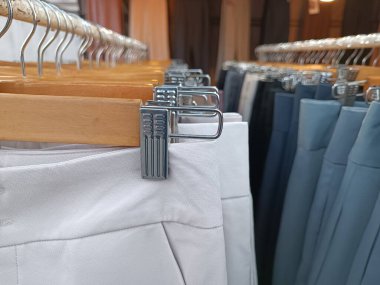 Close-up of neatly arranged formal trousers hanging on wooden hangers with metal clips in a clothing store. Showcasing variety in light and dark shades, ideal for a fashion or retail display concept