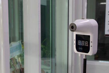 Wall-mounted infrared thermometer scanner in a modern building entrance, designed for non-contact body temperature measurement to enhance health safety and COVID-19 screening protocols
