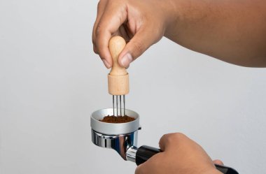 Hand using a coffee distributor tool to evenly level ground coffee in a portafilter for perfect espresso brewing, professional barista technique for specialty coffee preparation at home or caf