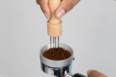 Hand using a coffee distributor tool to evenly level ground coffee in a portafilter for perfect espresso brewing, professional barista technique for specialty coffee preparation at home or caf