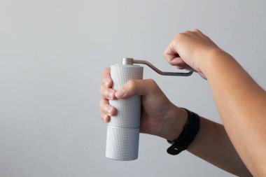 person's hands operating a white, minimalist manual coffee grinder, preparing for brewing pour-over or fresh coffee at home. Self-preparation of coffee beans for an aromatic and fresh coffee