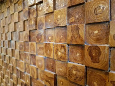 Close-up view of a decorative wooden wall made from cross-cut timber blocks, showcasing natural wood grain patterns and annual rings in various shades of brown. Ideal for backgrounds, textures, and architectural design inspirations