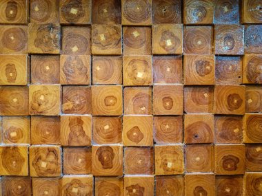 Close-up view of a decorative wooden wall made from cross-cut timber blocks, showcasing natural wood grain patterns and annual rings in various shades of brown. Ideal for backgrounds, textures, and architectural design inspirations