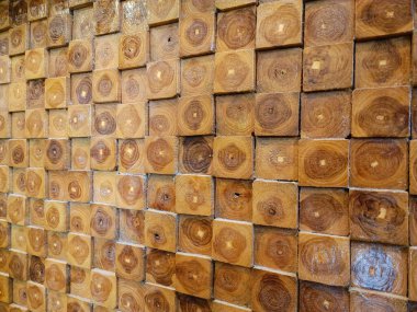 Close-up view of a decorative wooden wall made from cross-cut timber blocks, showcasing natural wood grain patterns and annual rings in various shades of brown. Ideal for backgrounds, textures, and architectural design inspirations
