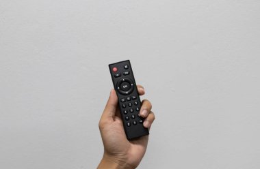 Hand holding a TV remote control and pressing the power button against a blank wall, concept of home entertainment, smart television, streaming and lifestyle technology