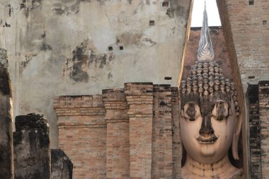Ancient Buddha statue partially hidden behind old brick walls at Wat Si Chum temple in Sukhothai Historical Park, Thailand, showcasing serene spiritual architecture and cultural heritage