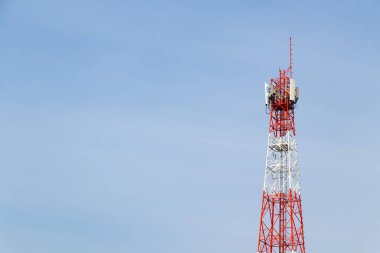 Red and white communication tower with multiple antennas against a clear blue sky, used for broadcasting, cellular network, and telecommunication signals