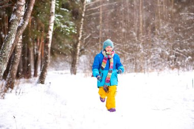 Parlak kış kıyafetleri içindeki mutlu çocuk kışın kar parkında koşar.