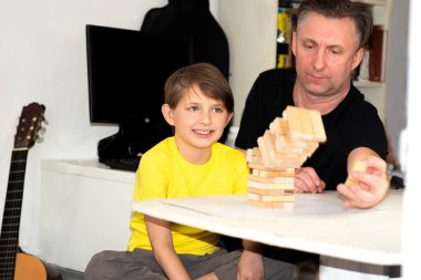 Baba ve oğul bir masa oyunu oynuyorlar. Mutlu çocuk, tahta kuleden tuğla çıkaran babaya benziyor.