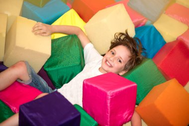 Mutlu çocuk köpüklü yumuşak renkli küplerin üzerinde yatıyor.