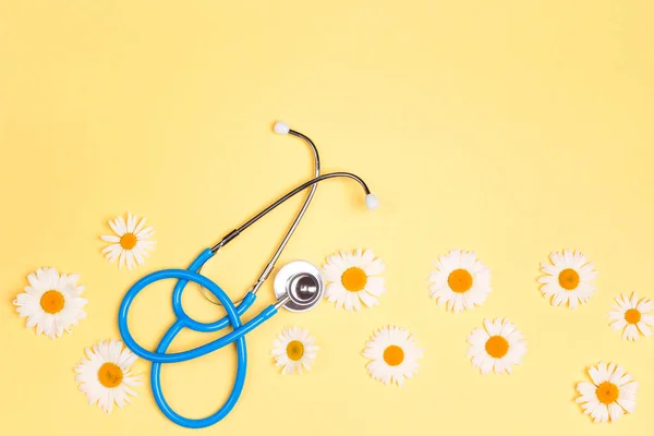 Blue stethoscope with chamomile flowers on yellow background. Top view with copy space. National Doctor's day. Happy nurse day.