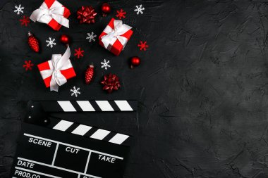 Noel süsleri ve siyah arka planda fotokopi alanı olan hediyelerle dolu bir film alkışlama tahtası. Kış tatili sineması.