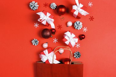 Kırmızı kağıttan alışveriş torbası, Noel süsleri ve kırmızı arka planda hediye. Üst manzara, düz uzanma.