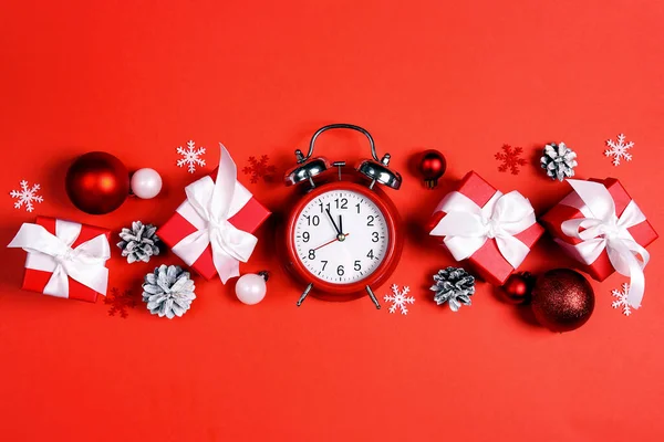 闹钟上有圣诞装饰品和红色背景的礼物 新年定时器该庆祝了 图库图片