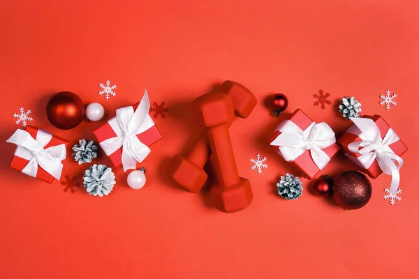 红色哑铃 带有冬季装饰和红色背景的礼物 带复制空间的顶级圣诞健身作品集 免版税图库图片