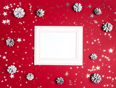Karla çevrili boş beyaz fotoğraf çerçevesi kırmızı arka planda çam kozalakları ve yıldızlar boyadı. Noel, Yeni Yıl, fotokopi alanı ile üst görünüm kavramı.
