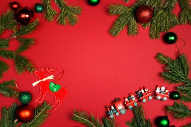 Kırmızı arka planda köknar dalları ve oyuncaklardan yapılmış Noel çerçevesi. Boşluğu kopyala, üst görünüm, düz katman.