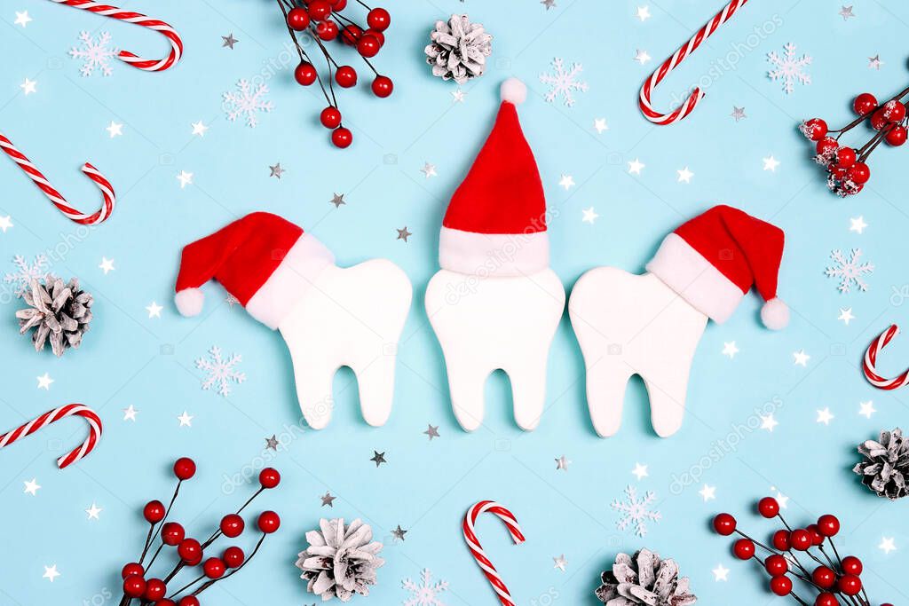 White teeth in santa hats surrounded by christmas decorations on blue background. Dentist Merry Christmas and New Year concept. Top view, flat lay.