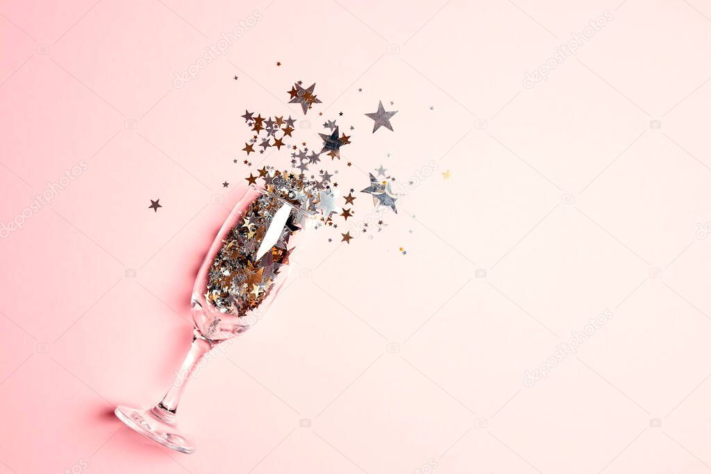 Champagne glass with golden star sequins splashing on pastel pink background. Top view with copy space. Party, and celebration concept.