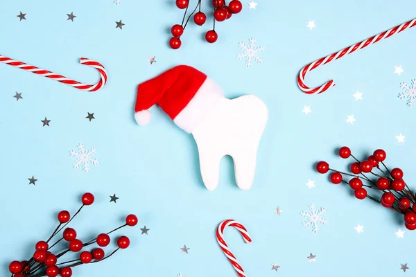 白色的牙齿戴着圣塔帽 周围是蓝色背景的圣诞装饰品 牙科医生圣诞快乐和新年的概念 免版税图库照片
