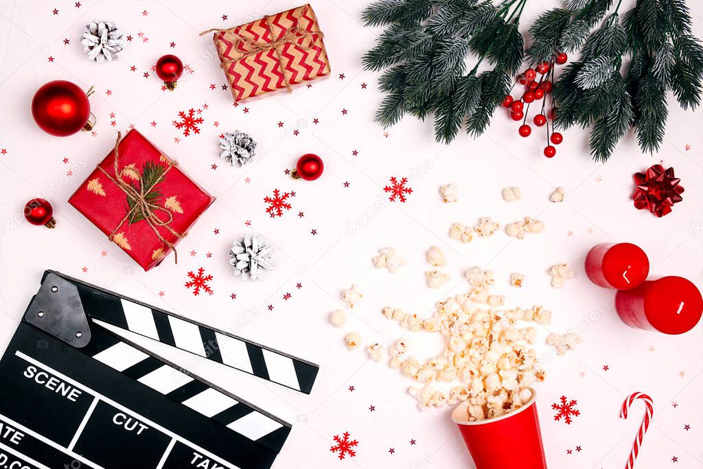 Movie clapper board with Christmas decorations, gifts and popcorn on white background. Cozy leisure time with a movie during the winter holidays.