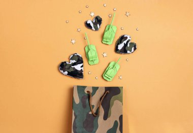 Origami kağıt tankları ve sarı arka planda kamuflaj kalpleri olan haki rengi bir alışveriş çantası. Anavatan Günü Savunucusu, 23 Şubat. 
