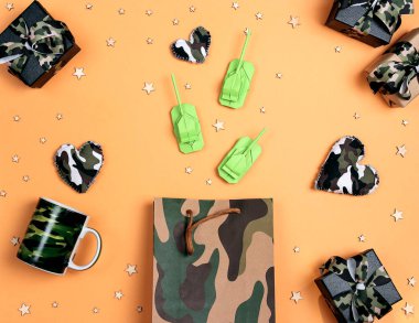Origami kağıt tankları, hediyeler ve sarı arka planda kamuflaj kalpleri olan haki rengi bir alışveriş çantası. Anavatan Günü Savunucusu, 23 Şubat. 
