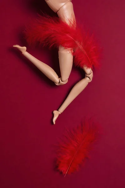 Legs of a plastic doll with a red feather on the belly. Women\'s health, menstruation and gynecology concept. Vertical red background.
