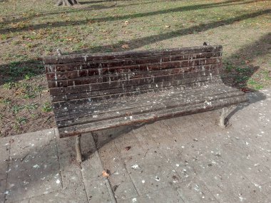 Wooden bench in the park covered by birds droppings, pigeon poop, Old wooden bench surface damaged by birds droppings showing the mess made by the birds.