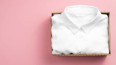 İçinde giysiler olan bir karton kutu. Ürünler online, teslimat konsepti. Pembe arka plan. Üst görünüm, alanı kopyala.