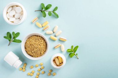 Kavanozlarda vitaminler ve bitkisel takviyeler. Mavi arka planda yeşil bir bitki var.