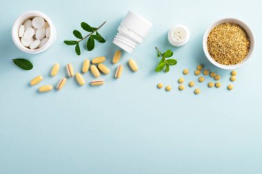 Kavanozlarda vitaminler ve bitkisel takviyeler. Mavi arka planda yeşil bir bitki var.