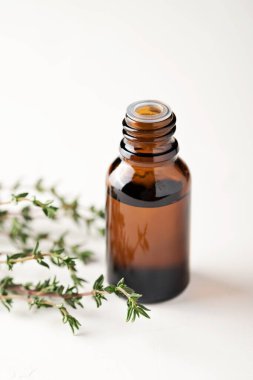 Cam bir şişedeki kekik yağı arka planda yakın plan. Kekik dalları masanın üstünde..