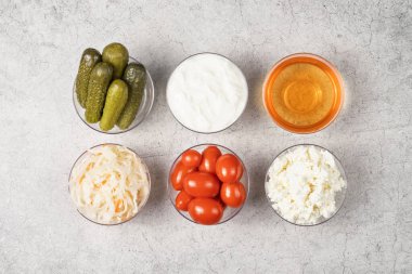 Mide sağlığı için çeşitli mayalanmış gıdalar. Gri arka planda kaseler. Salatalık, domates, lahana turşusu, yoğurt, süzme peynir, elma sirkesi..