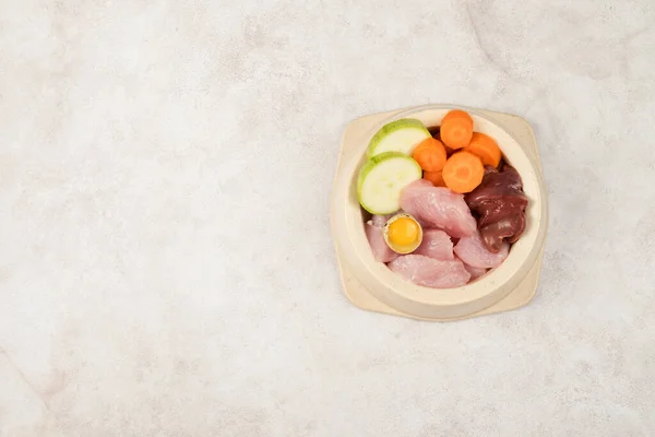 A bowl of natural products for feeding pets. Meat, liver, vegetables, quail egg. View from above. Copy space.