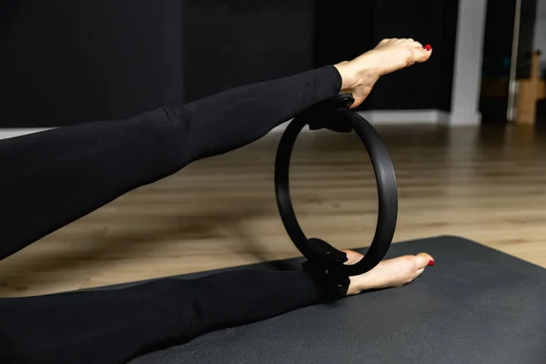 Jambes minces d'une femme athlétique serrer un anneau de pilates. Fitness avec pilates cercle magique dans les jambes, entraînement en vêtements de sport, salle de gym — Photo