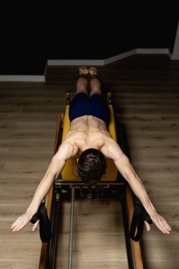 Sporty man doing exercises on pilates reformer training machine. Working out wearing sportswear, gym.