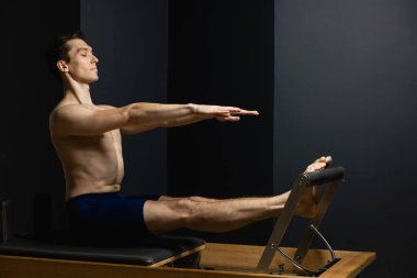 Sporty man doing exercises on pilates reformer training machine. Working out wearing sportswear, gym.