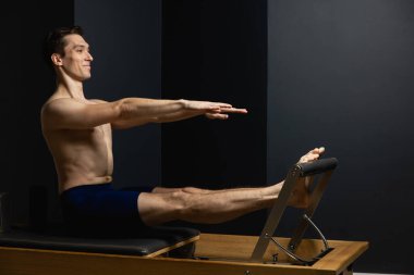 Sporty man doing exercises on pilates reformer training machine. Working out wearing sportswear, gym.