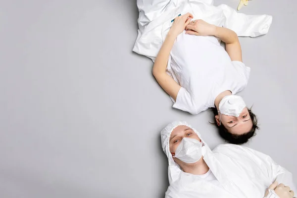 Двоє втомлених лікарів чоловічої та жіночої статі в захисному костюмі на підлозі, виснажених у боротьбі з пандемією ковадла-19 Стокове Фото