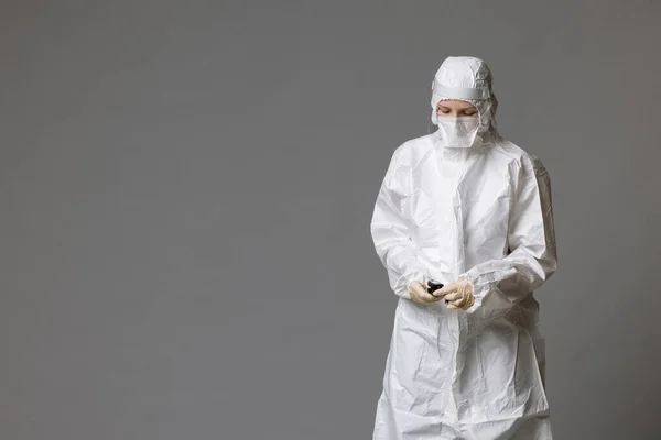 Medico stanco indossando maschera e guanti in ospedale in tempi coronavirus, controllando il suo smartphone . Foto Stock Royalty Free