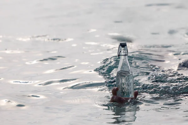Пляшка з чистою водою в руці в океані і кружляє навколо нього Стокове Фото