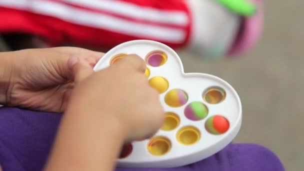 As mãos de menina de criança que jogam com o brinquedo antistress de silício popular estouram-no e covinham simples. Close-up — Vídeo de Stock